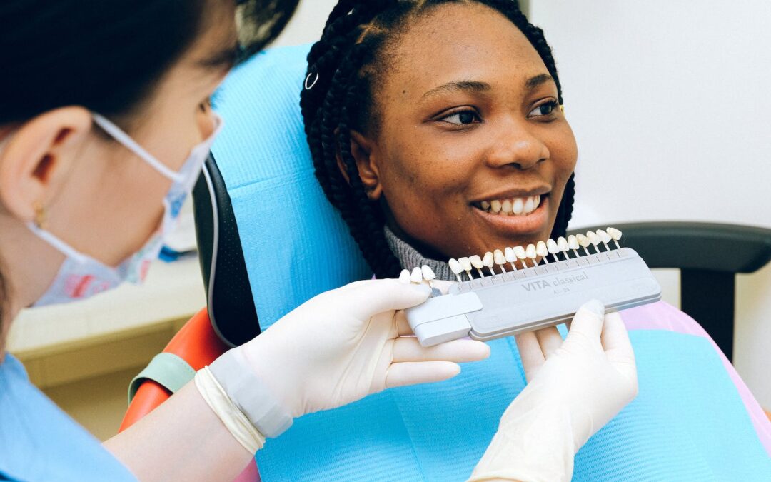 Cheerful black woman sitting in dental chair of modern dentist office and checking teeth implant while looking away