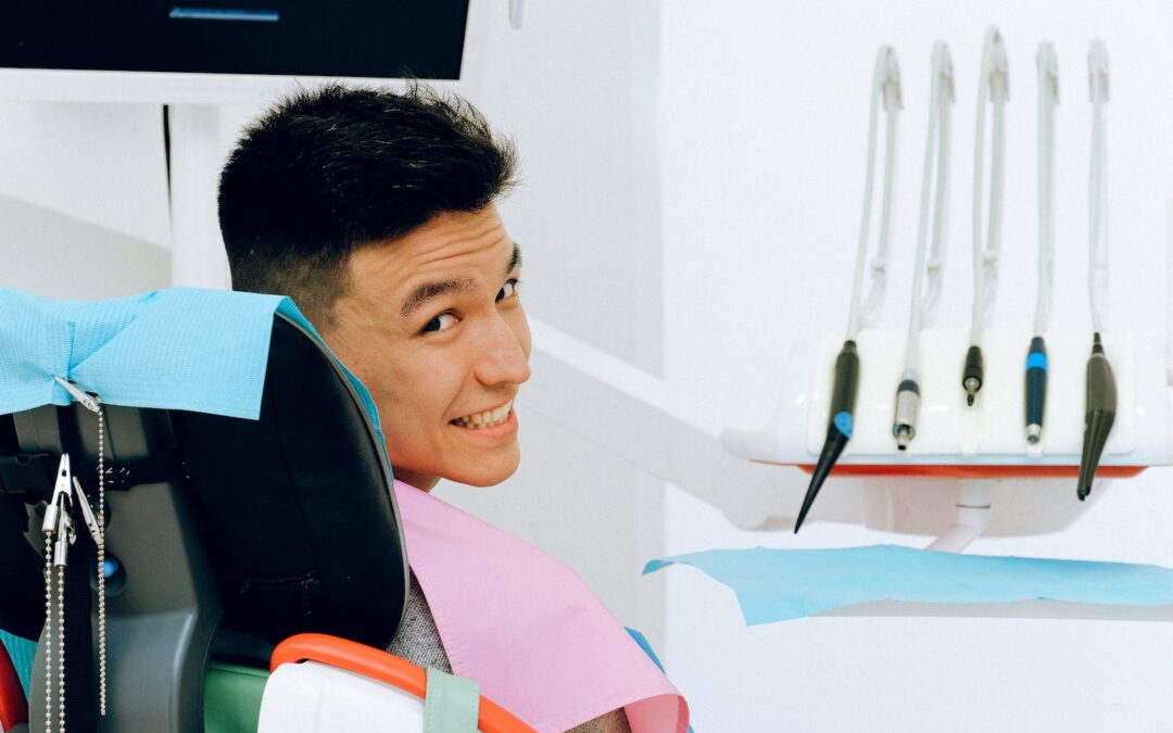 Back view of smiling ethnic man sitting in chair of dentist while preparing for treatment in modern clinic and looking over shoulder at camera